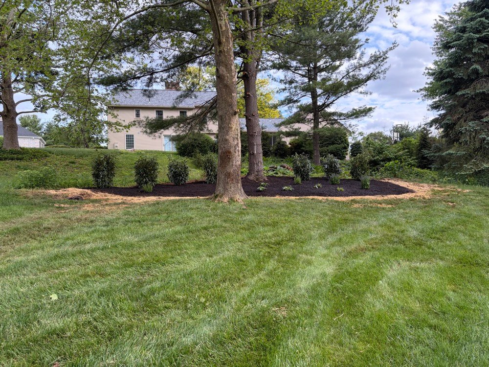 Crew member trimming along a stone wall border in a large backyard