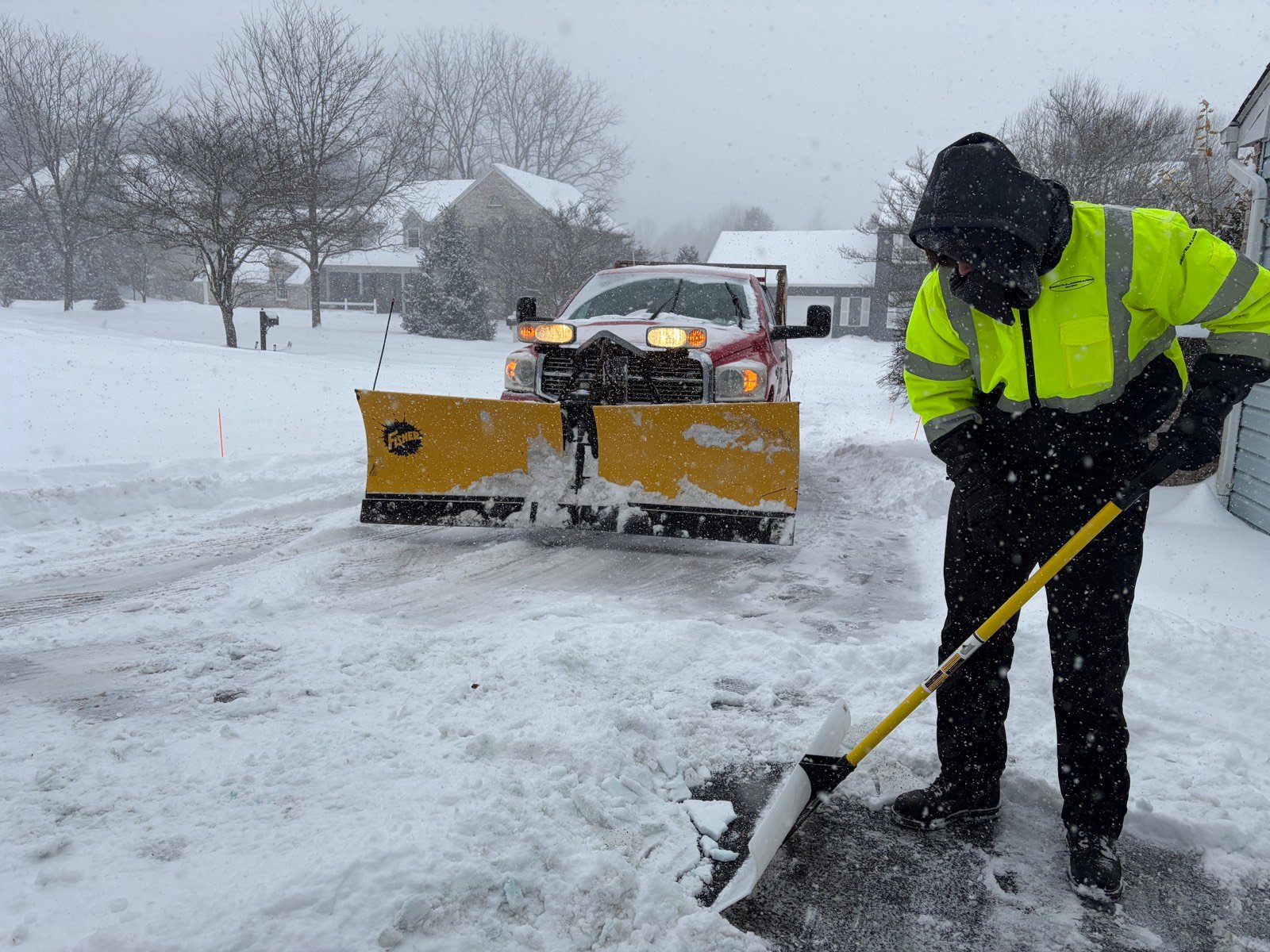 Bechtel's Landscaping plow truck and crew member clearing a driveway during a snowstorm