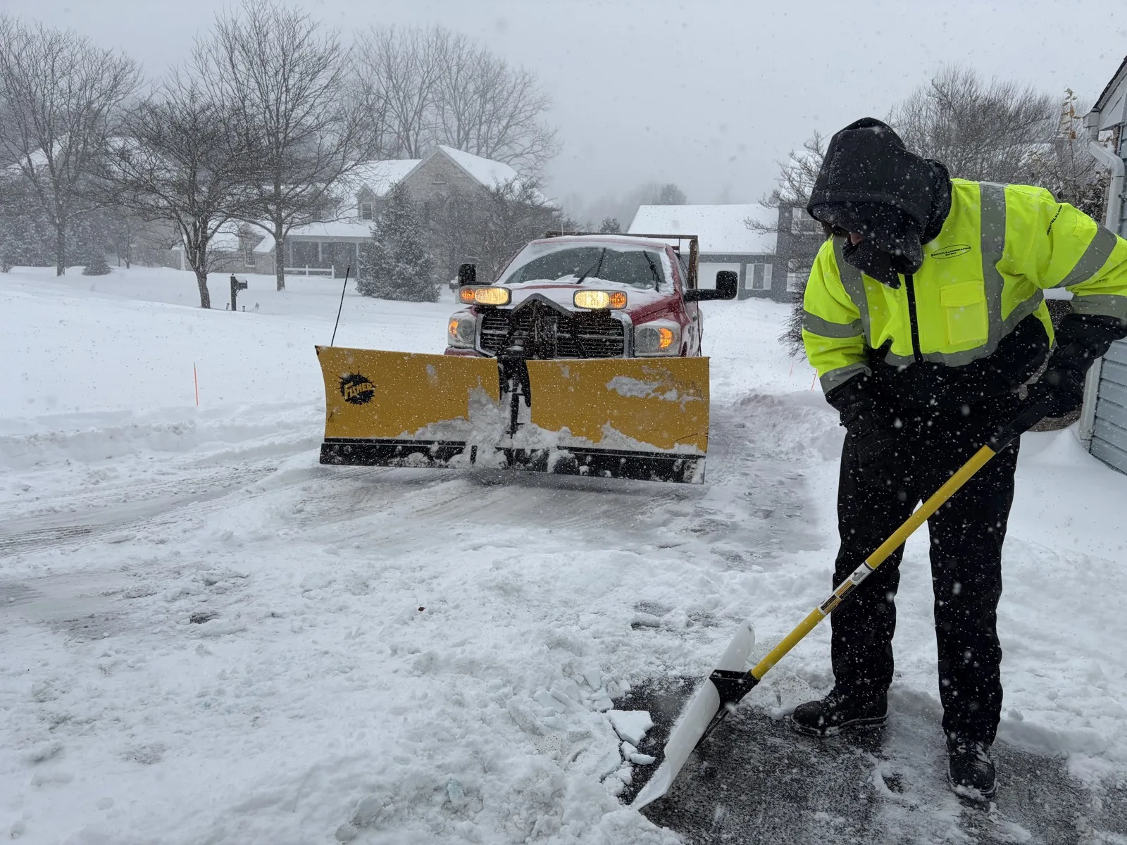 Bechtel's Landscaping plow truck and crew member clearing a driveway during a snowstorm